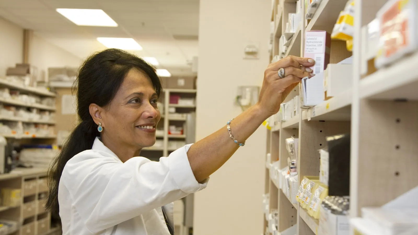 Apotheekmedewerker pakt een doosje medicijnen van een schap.