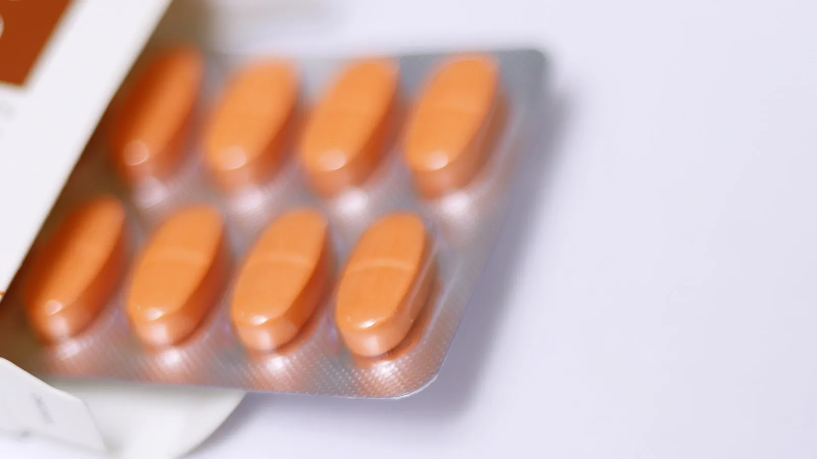 Doordrukstrip met oranje tabletten naast een medicijndoosje.