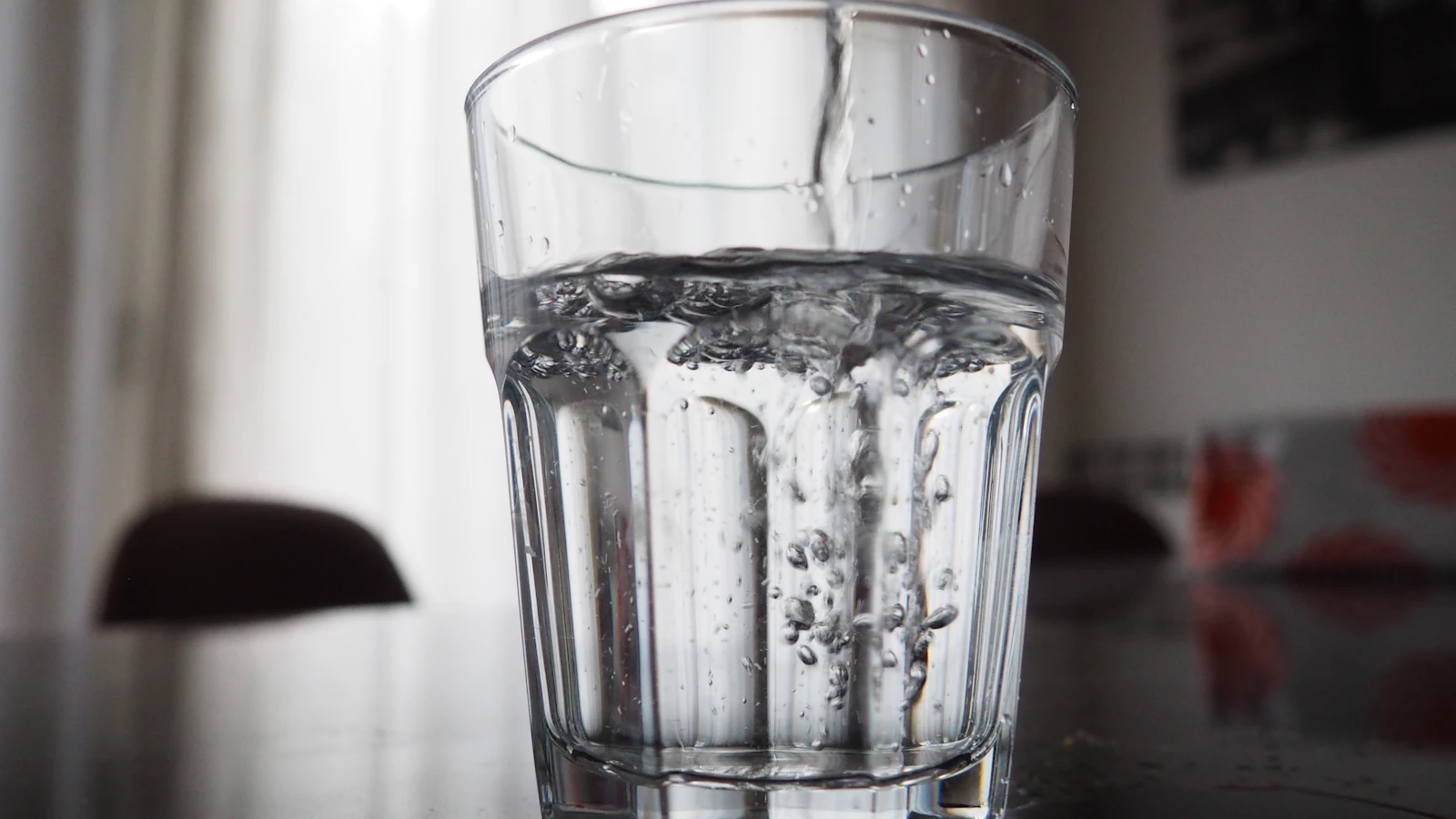 Een helder glas dat met water wordt gevuld op een tafel bij daglicht.