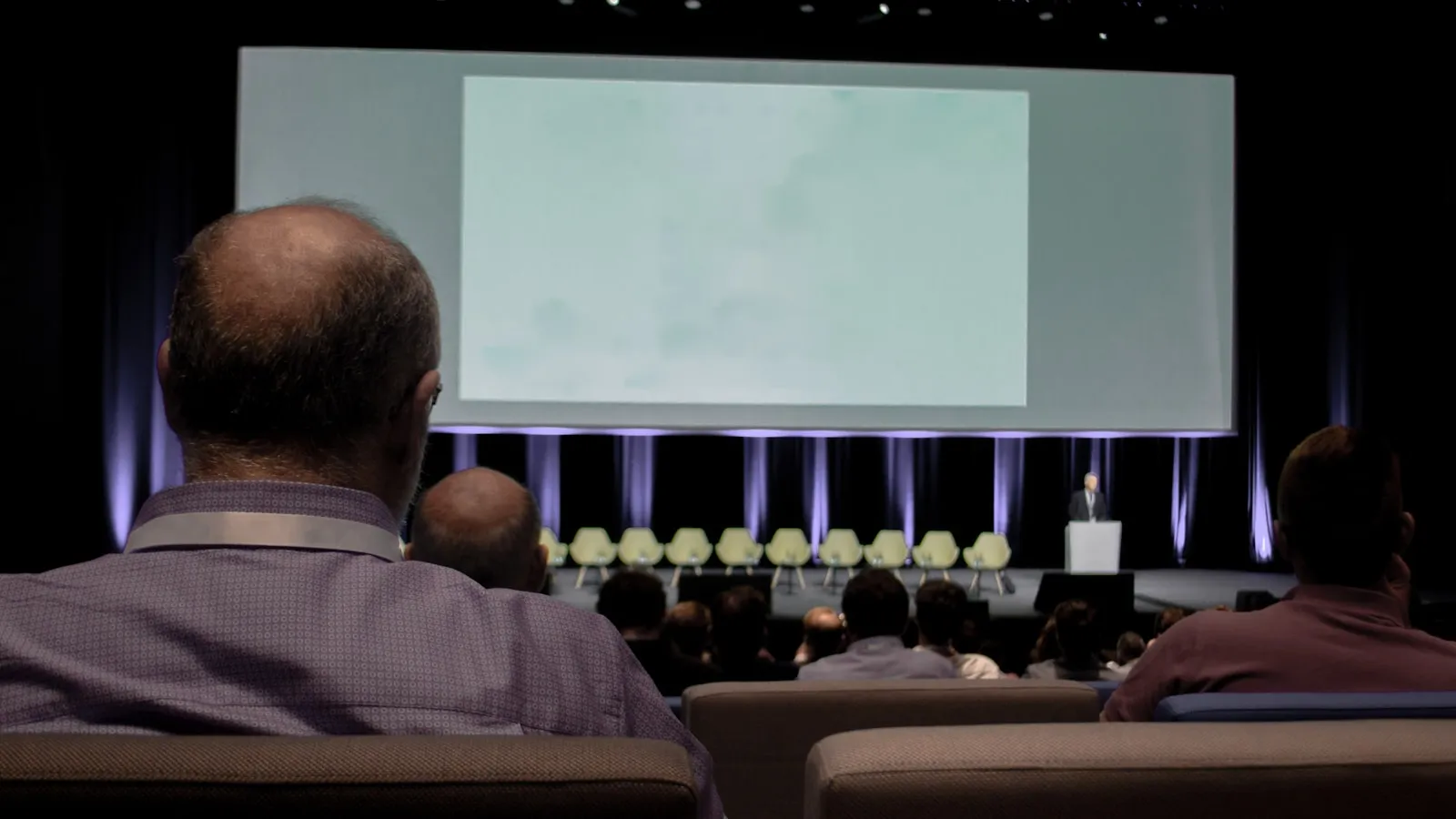 Een man van achteren gezien in een zaal, met een dunner wordende kruin.