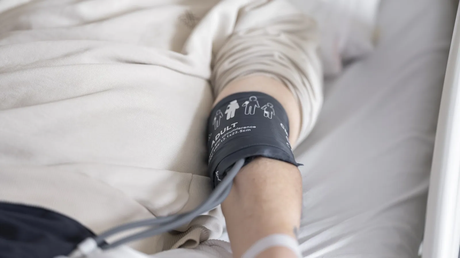 Een arm met een opgeblazen bloeddrukmanchet die op bed rust.