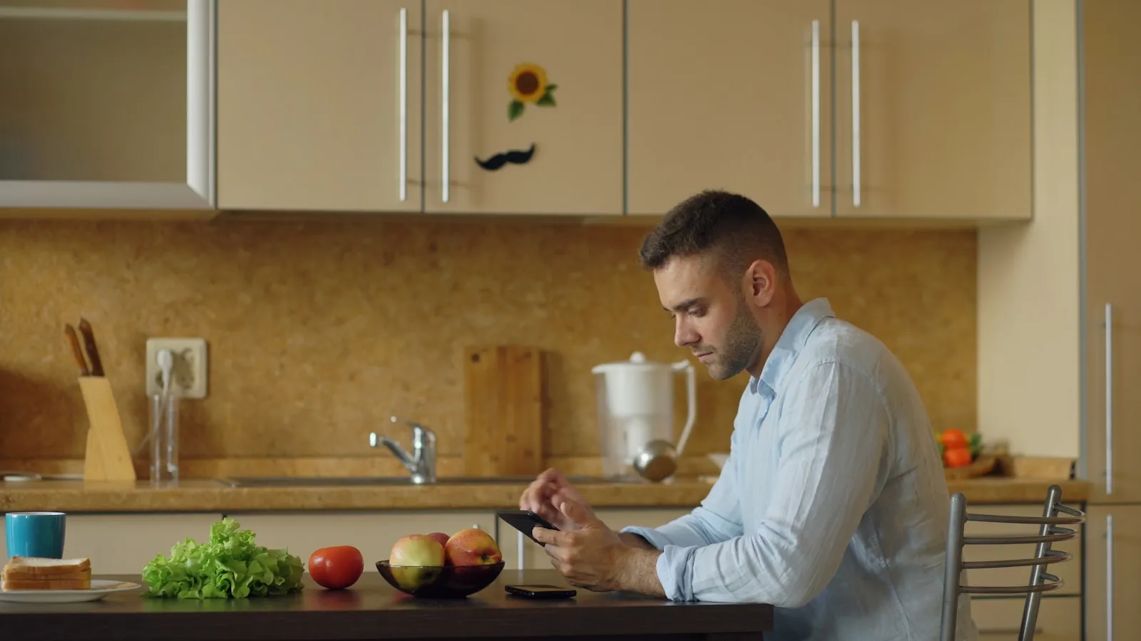Man van in de dertig zit aan de keukentafel met verse groente en fruit voor zich.
