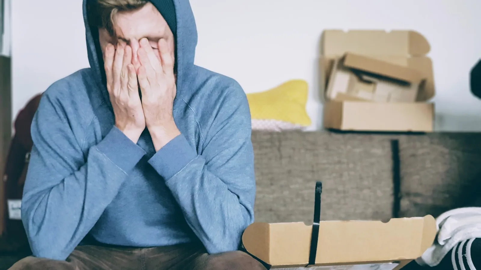 Vermoeide man in een blauwe hoodie met zijn handen voor zijn gezicht.