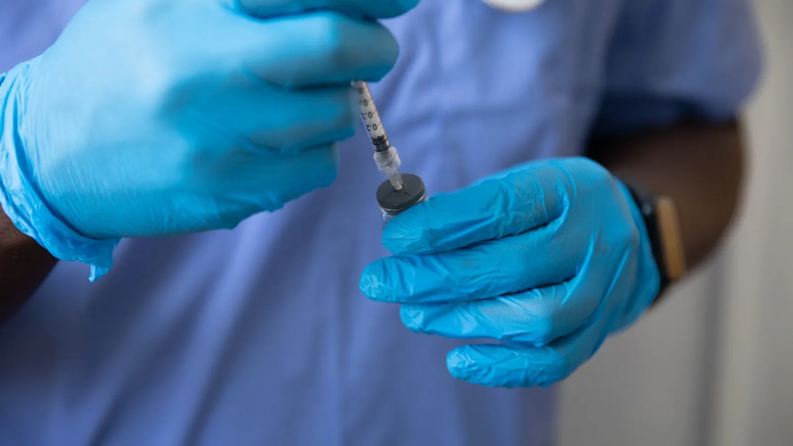 Handen met blauwe handschoenen trekken een injectiespuit op uit een flacon.