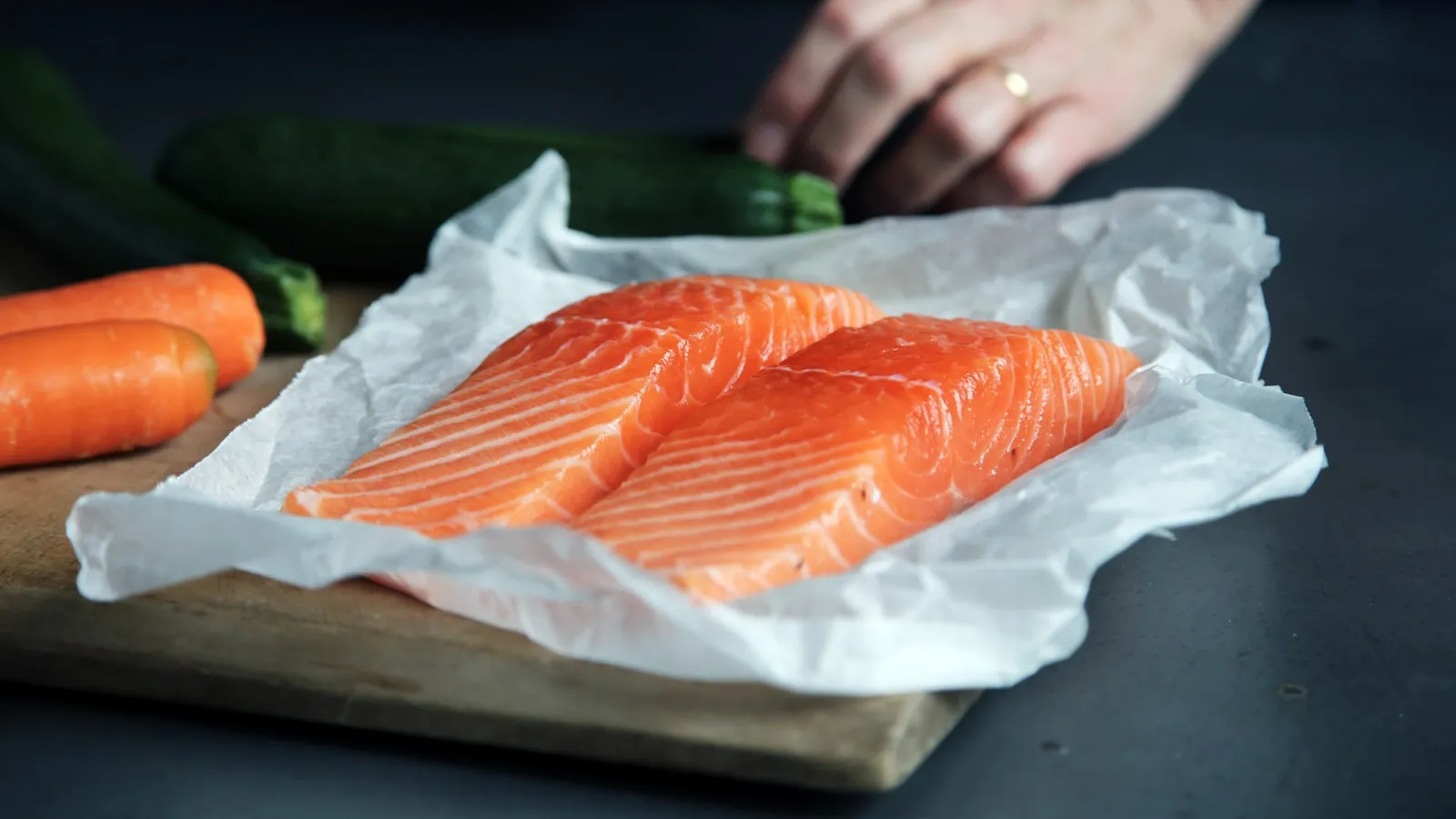 Verse zalmfilet op een snijplank met groente ernaast.