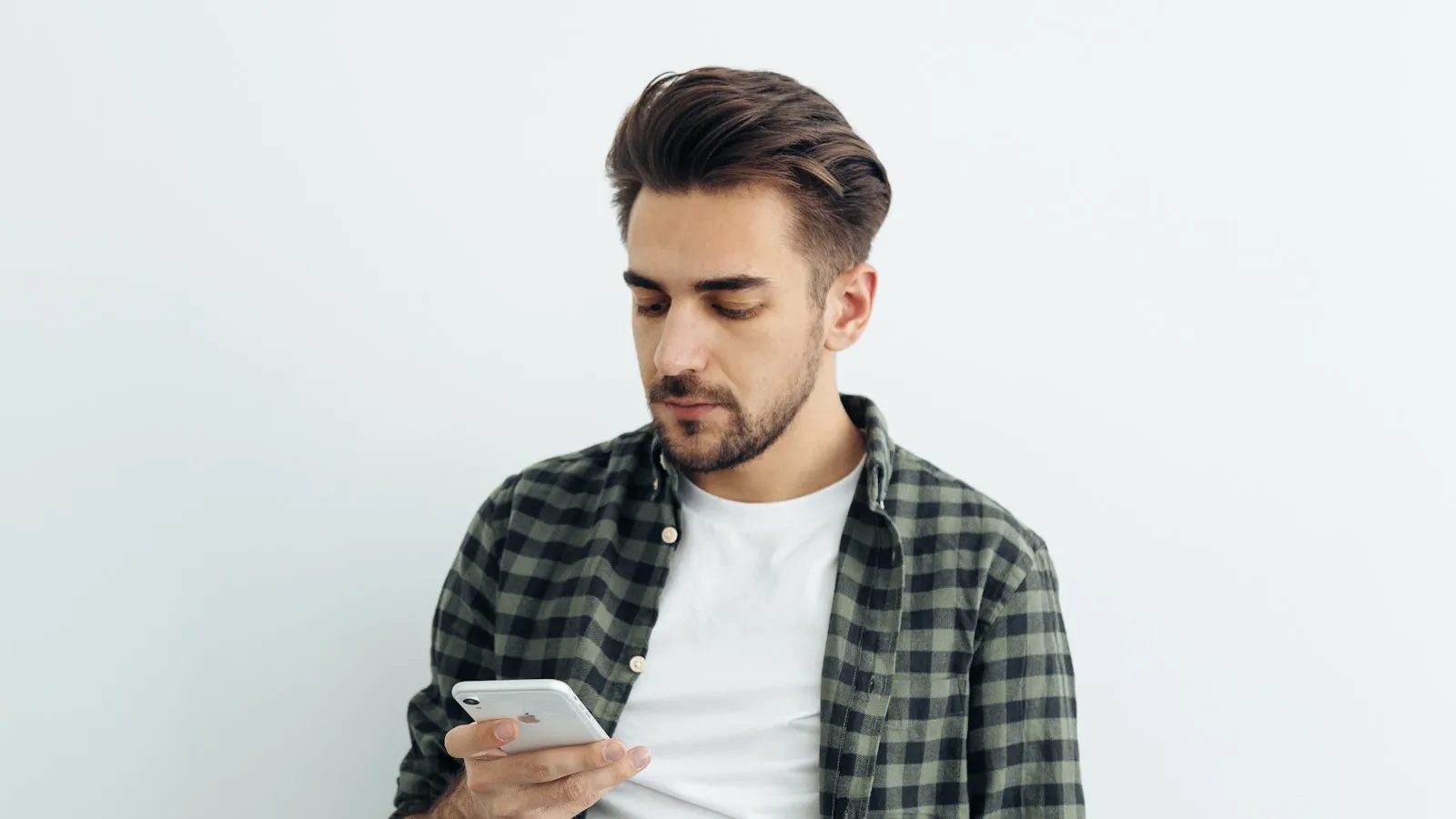 Man leest iets op zijn telefoon tegen een lichte achtergrond.