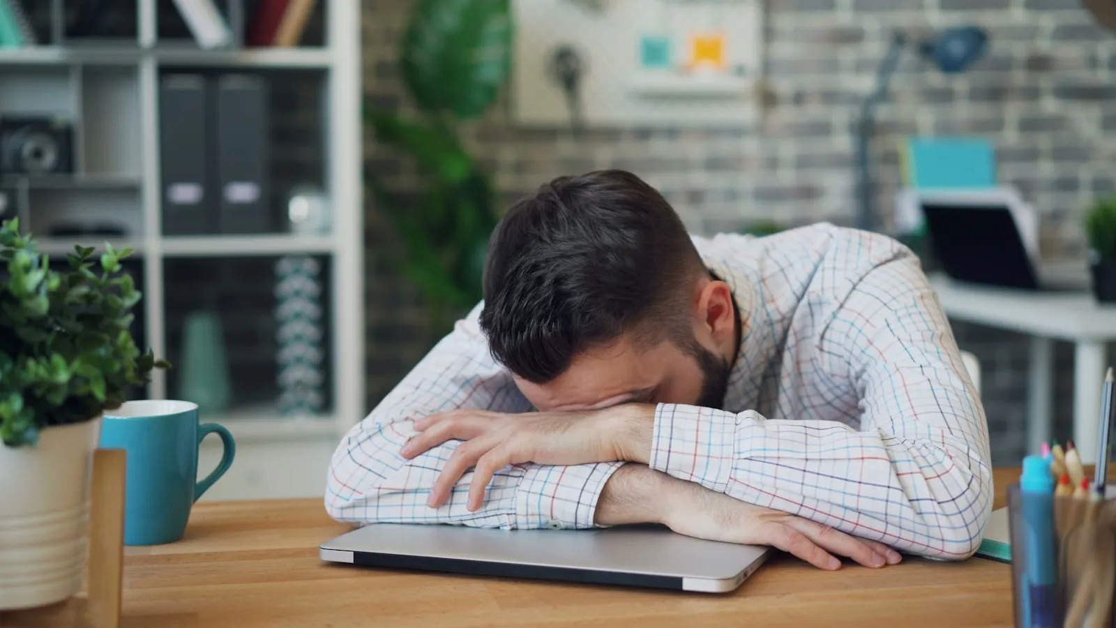 Man valt overdag in slaap op zijn laptop aan een bureau.