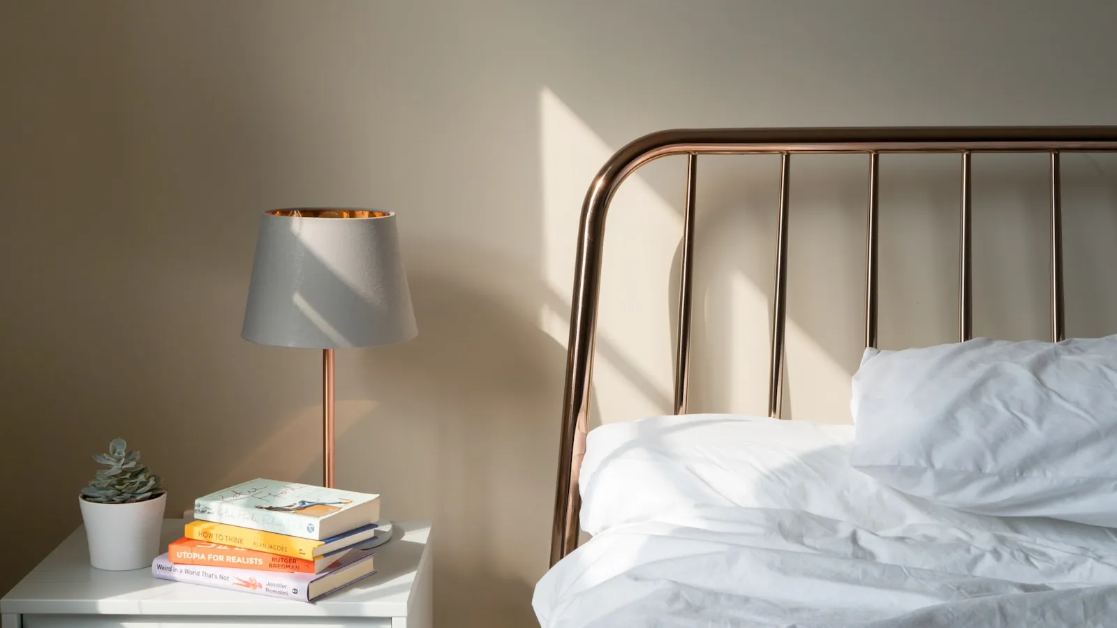 Nachtkastje met een lamp en boeken naast een opgemaakt bed.