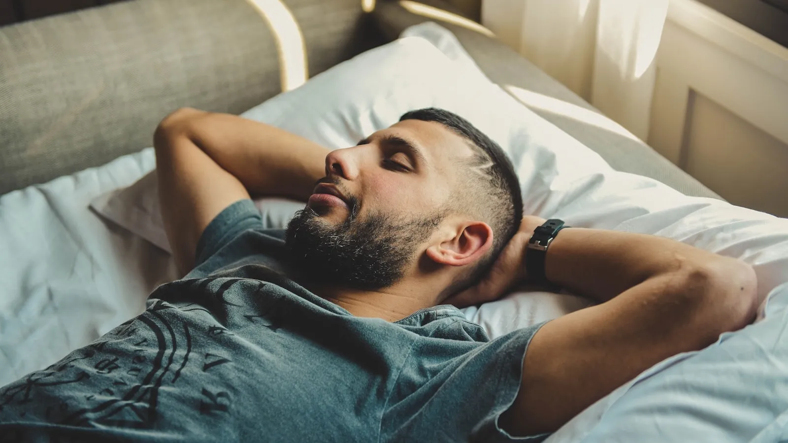 Man slaapt op zijn rug in bed bij zacht ochtendlicht.