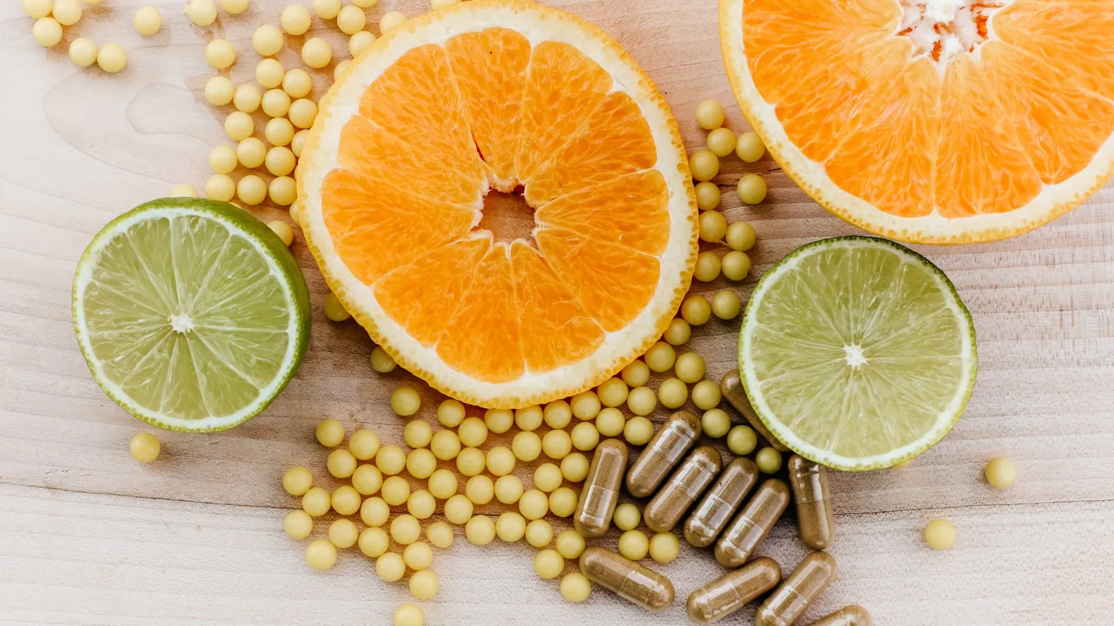 Sinaasappels, limoenen en supplementcapsules op een houten tafel.