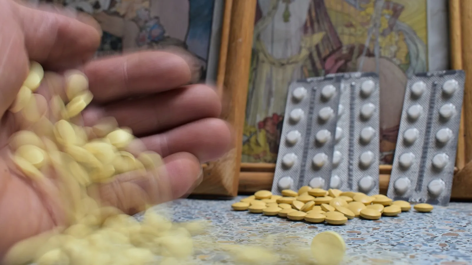 Hand laat gele tabletten vallen naast doordrukstrips op een tafel.