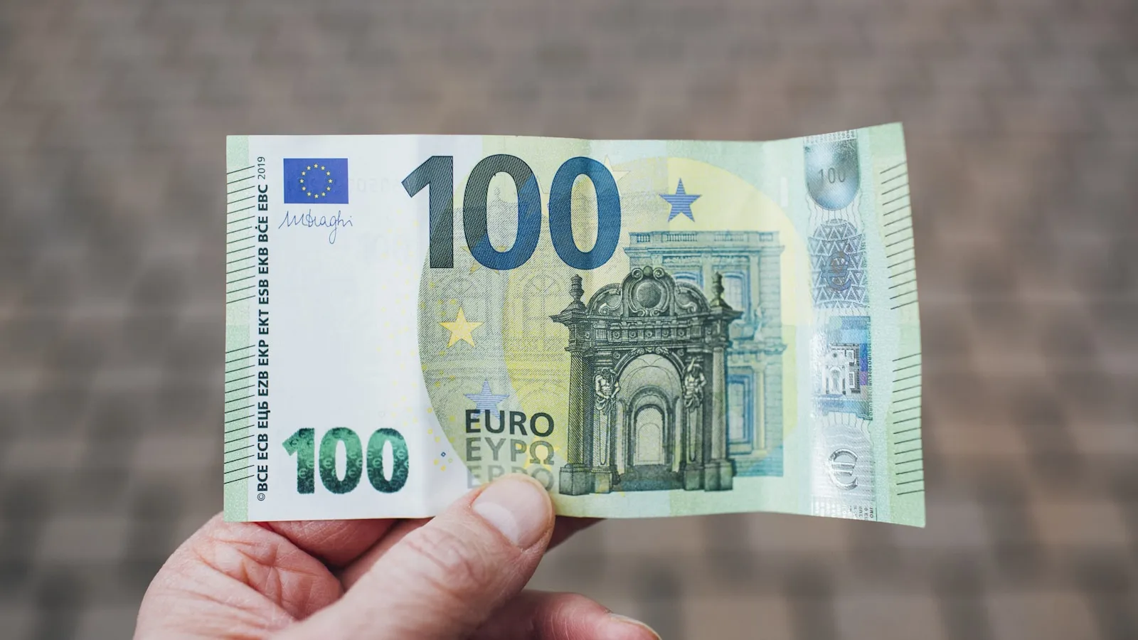 Hand houdt een biljet van honderd euro vast.