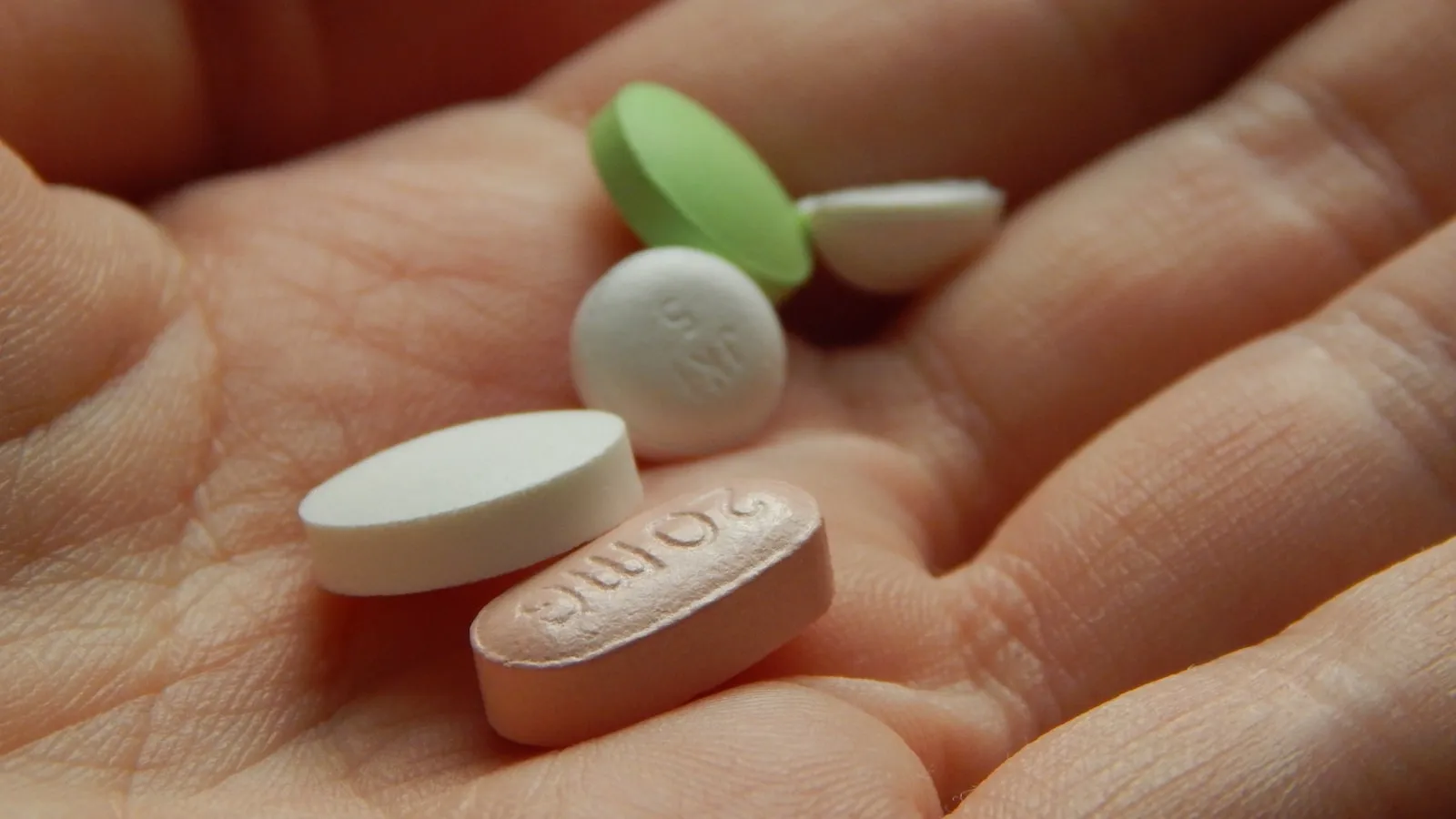 Hand met een aantal gekleurde tabletten en capsules.