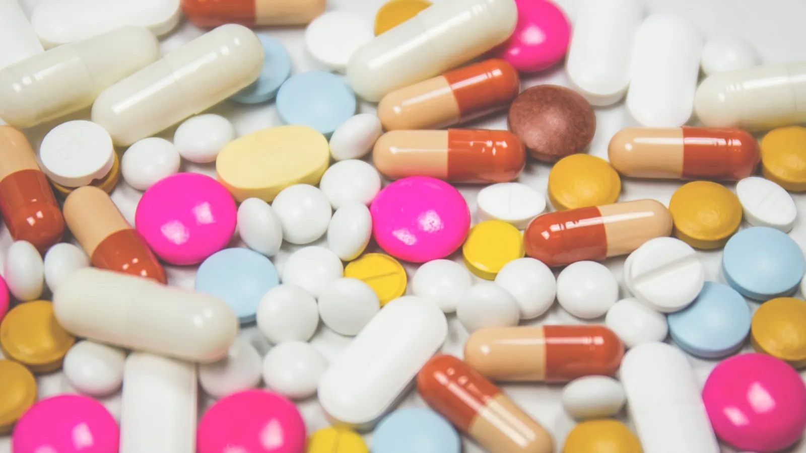 Losse vitaminepillen en capsules in verschillende kleuren door elkaar.